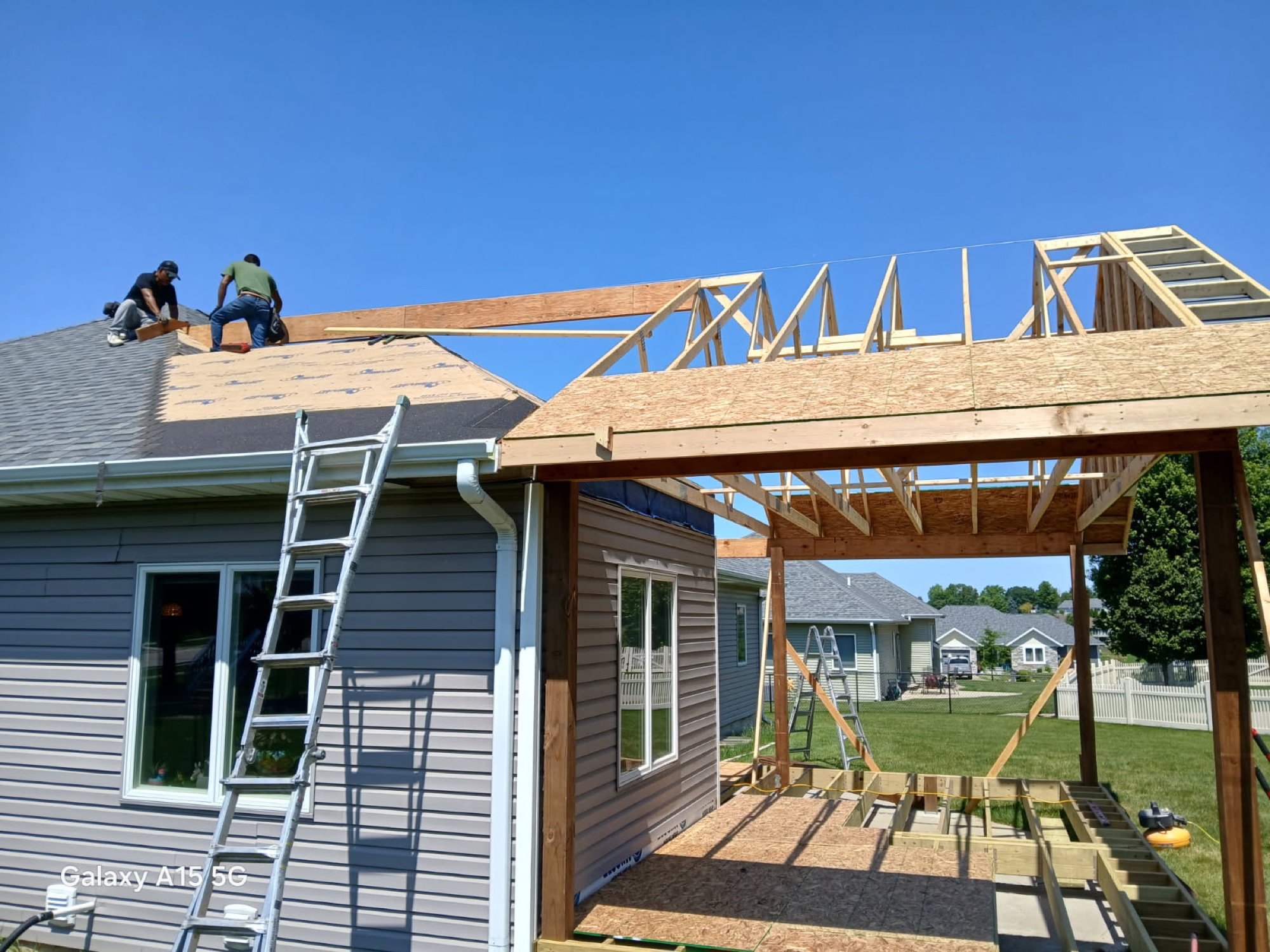 Crew framing the roof of a large room addition, trusses set against a clear sky