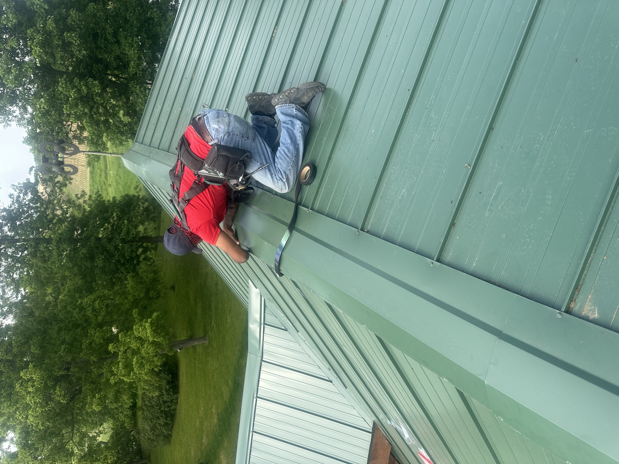 Crew member fastening the ridge on a green standing-seam metal roof