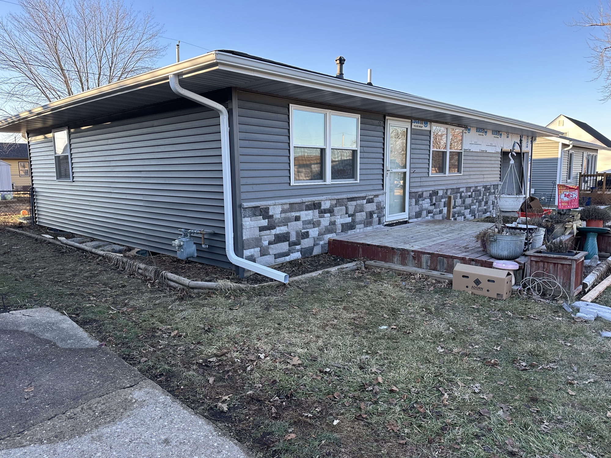 Finished home exterior with new gray siding, stone accent skirt and gutters